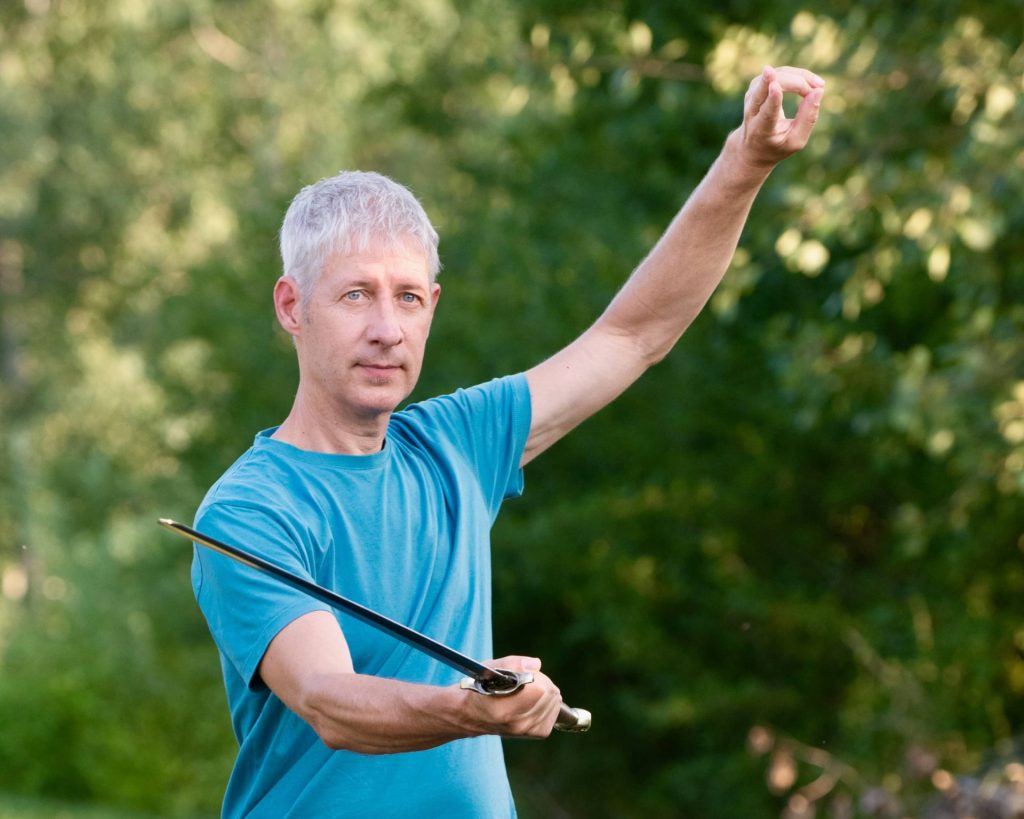 Person vor grünem Hintergrund mit Taiji Schwert Technik.