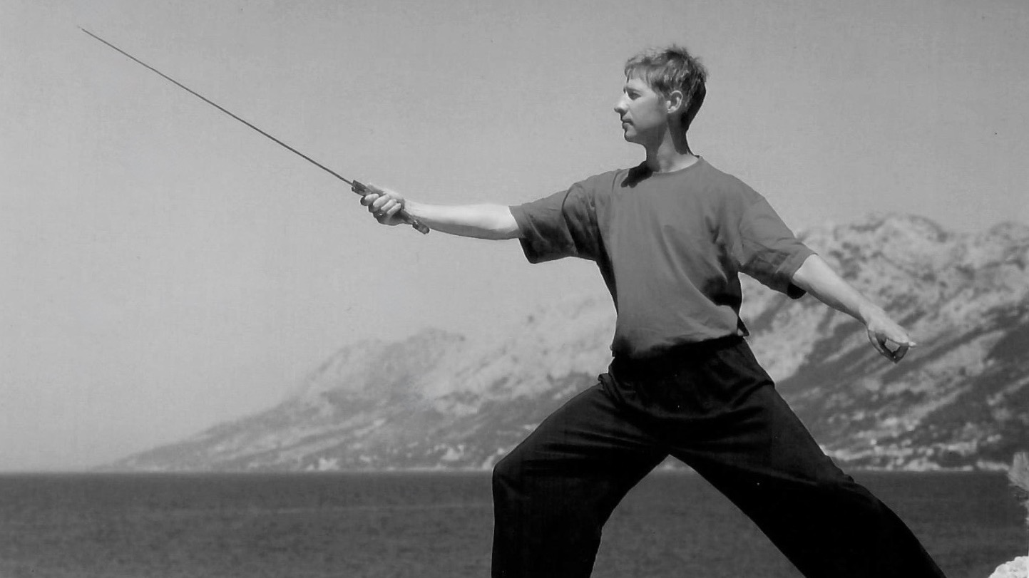 Person in Taiji-Schwert-Position vor Meeresküste.